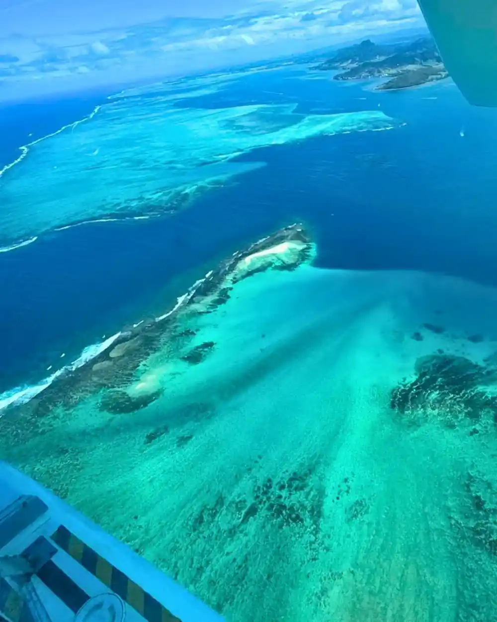 An elongated sandbank with surf breaking along it and deep blue beyond