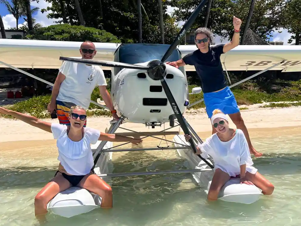 Four people posed on and beside the seaplane floats in shallow water