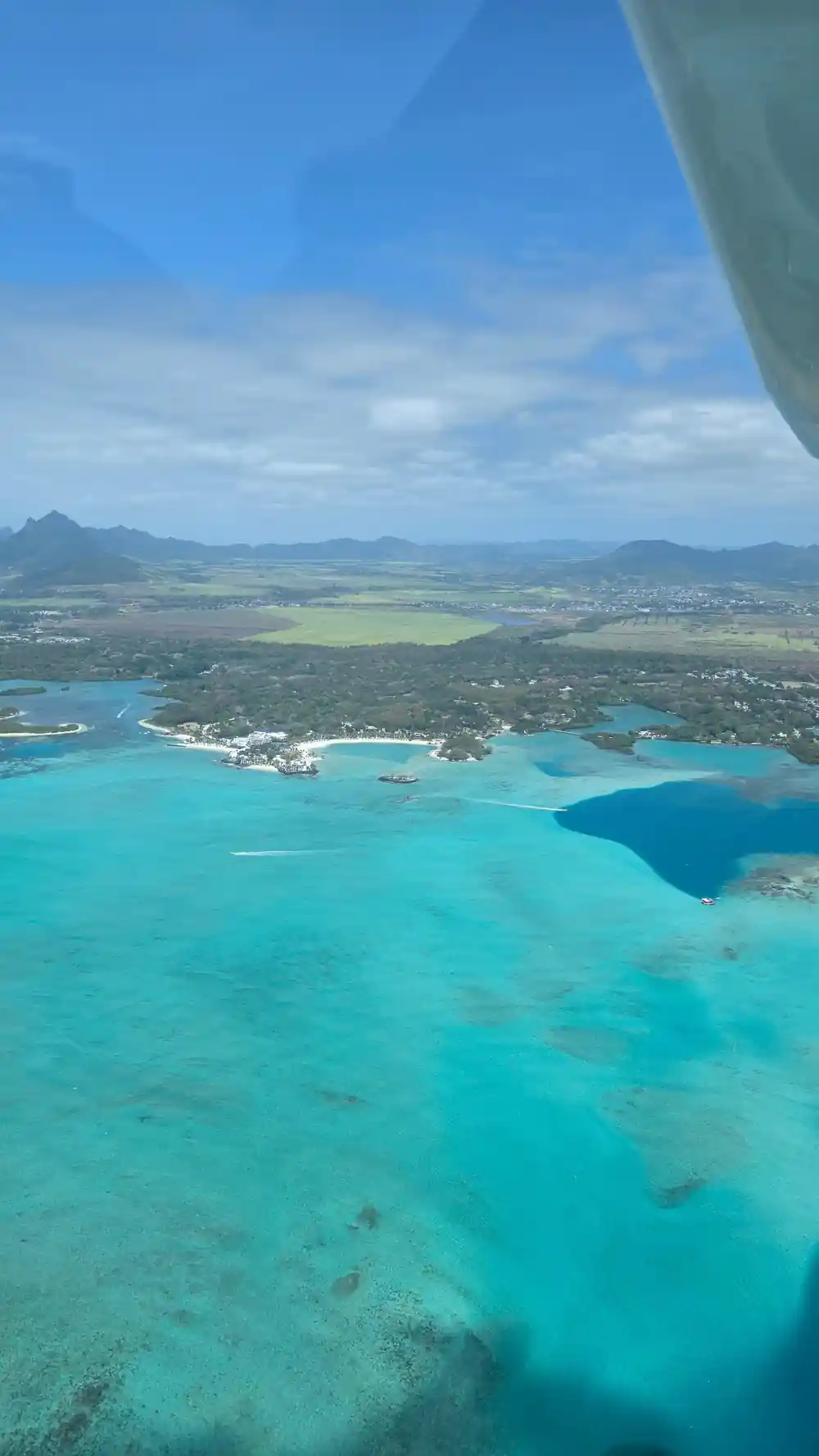 A green coastal plain with the mountain range behind and the lagoon in the foreground