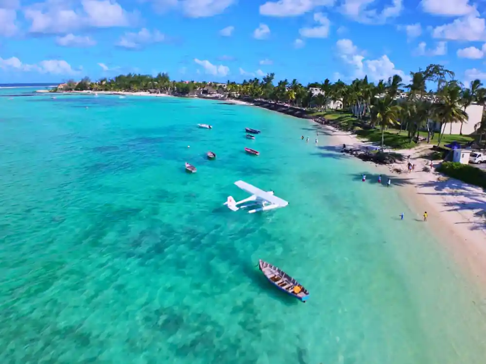 A hotel beach from the air with the seaplane moored offshore and a pirogue alongside