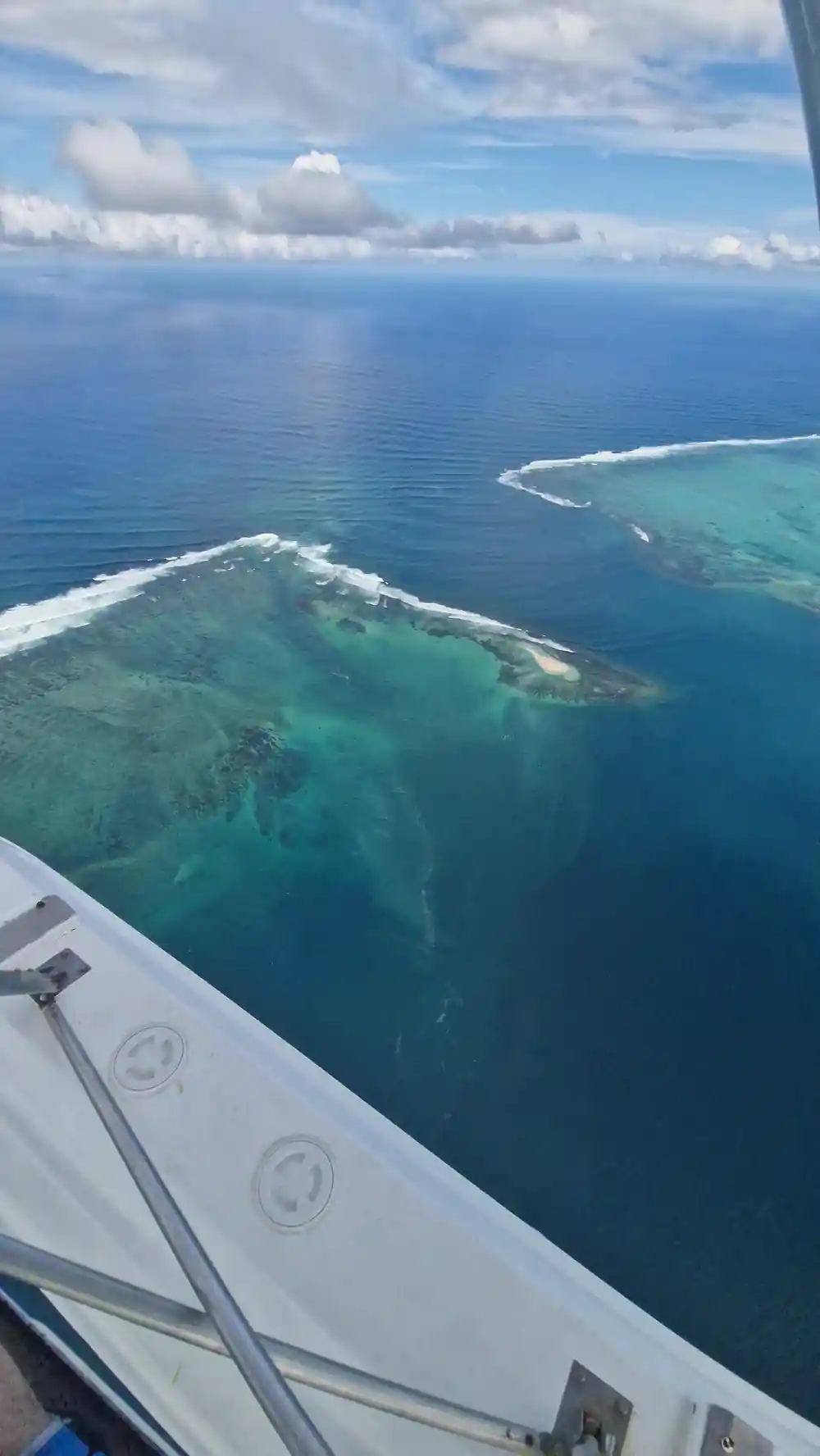 A long reef island with pale shallows, the wing in frame