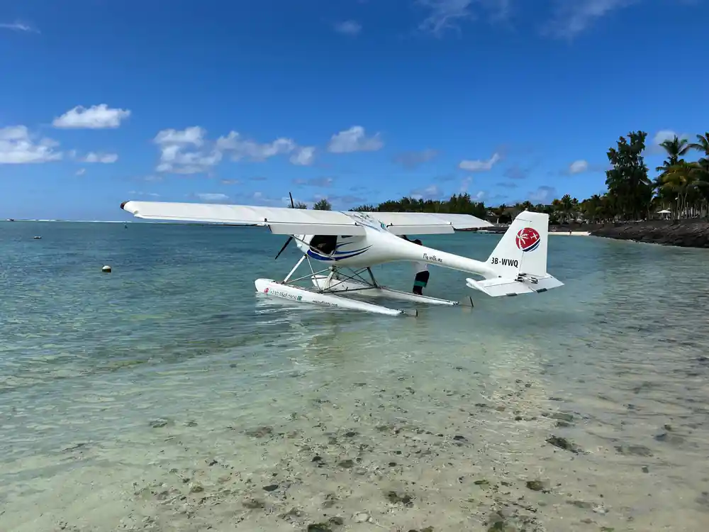 The seaplane on its floats in clear shallows with trees behind
