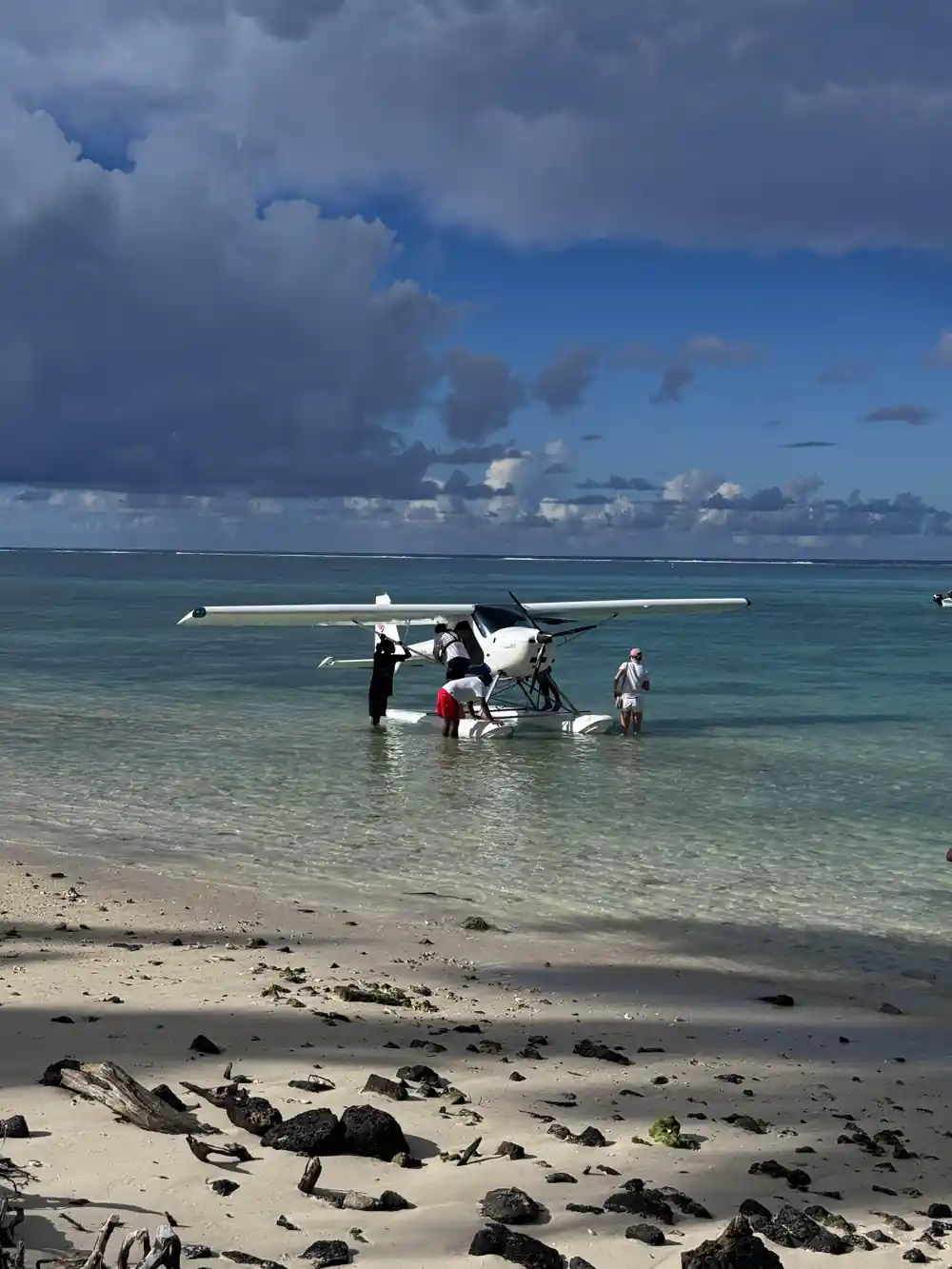 The seaplane on the water at a beach with crew standing beside it