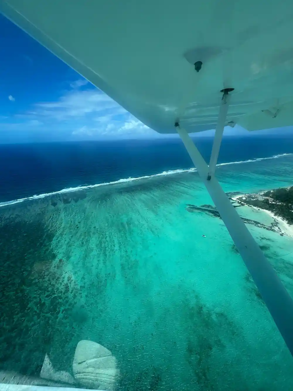 Sediment streaming off the reef shelf below the wing strut, with the sandbank beyond